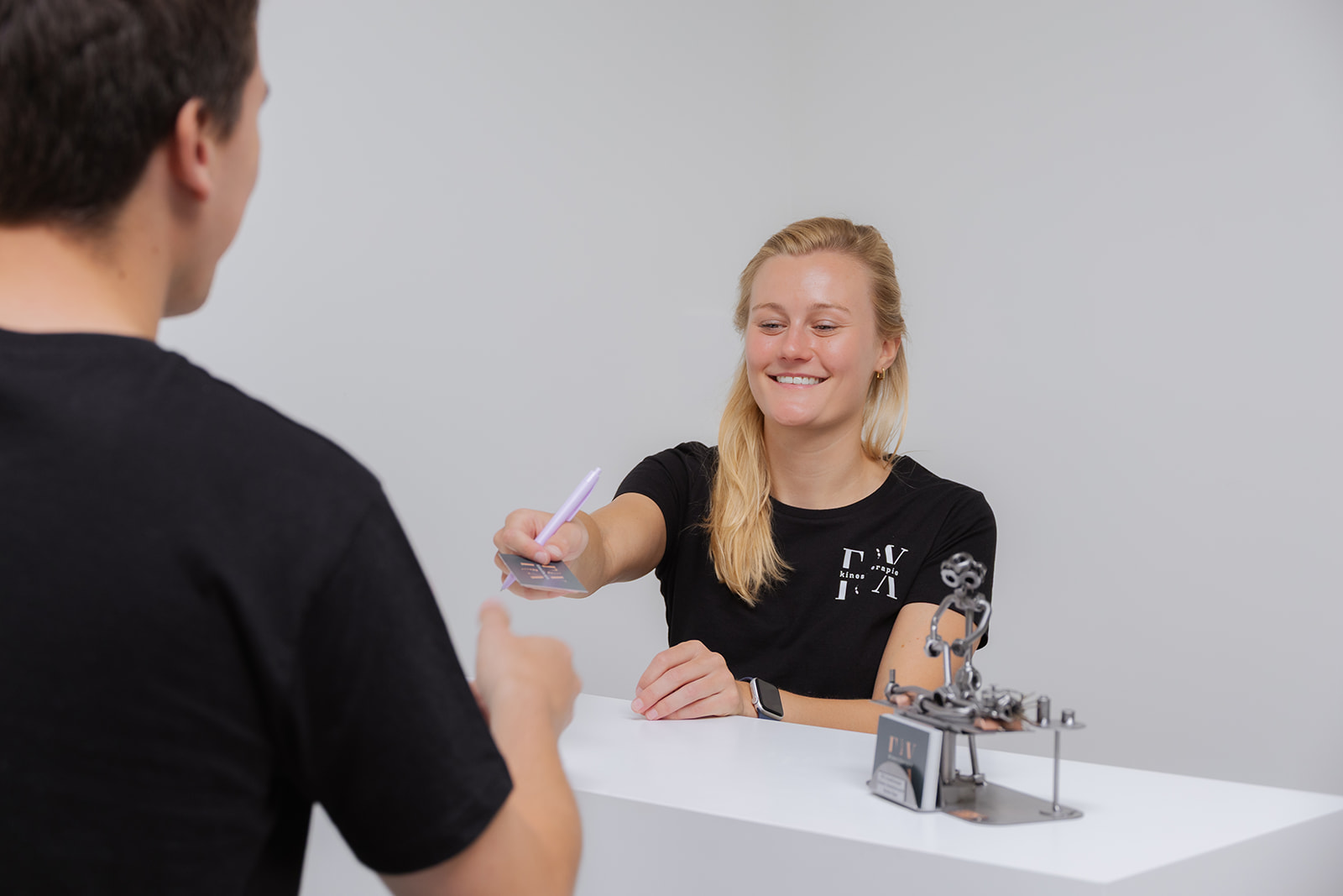 Patiënt aan de balie van de praktijkruimte met kinesitherapeut